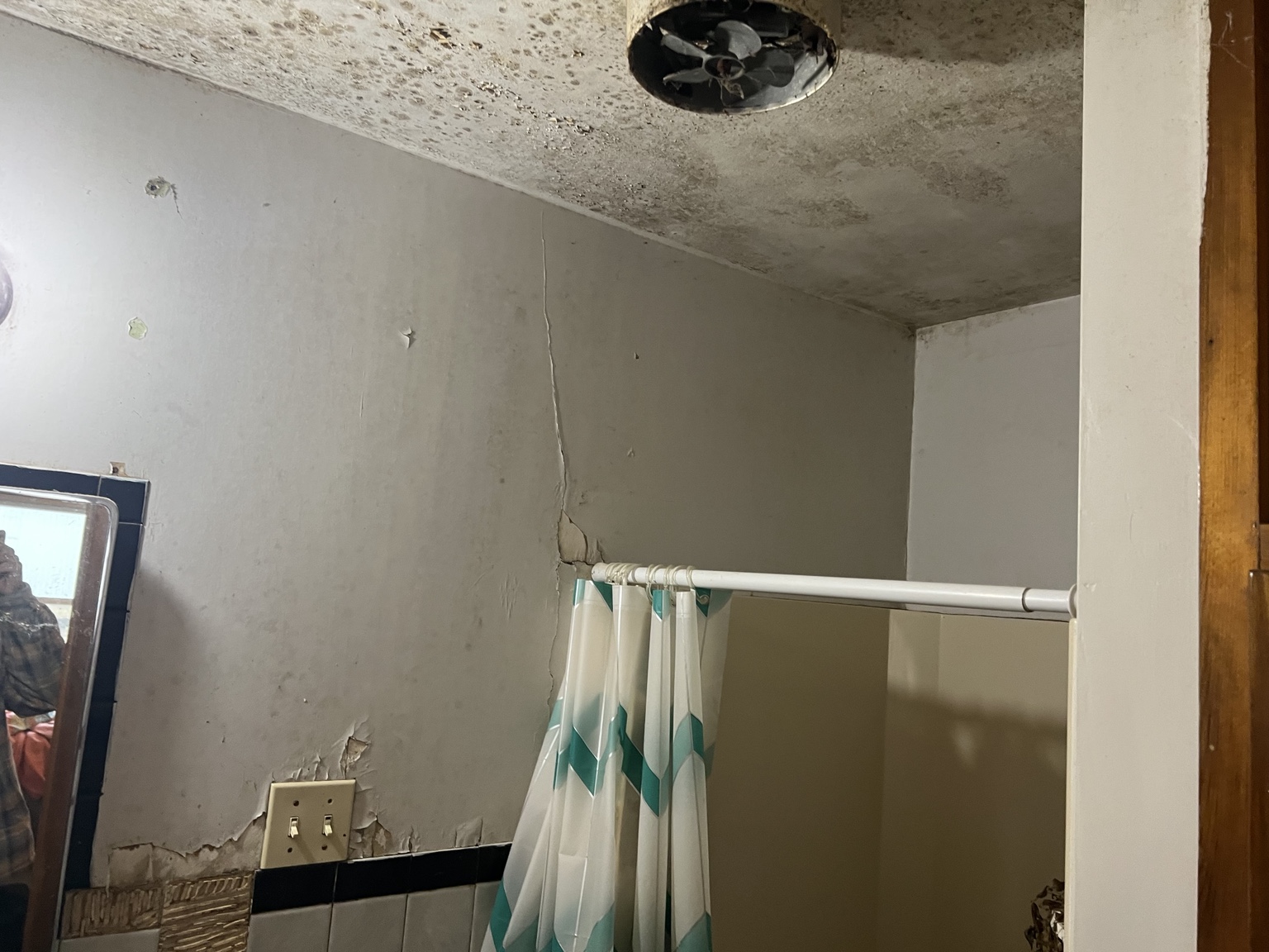 Bathroom corner with damaged wall and ceiling finishes, beside a shower curtain and wood cabinet.
