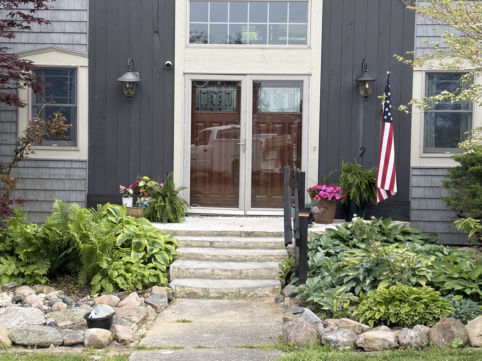 The same red double doors above a new concrete landing, with a dark handrail down the stone steps.