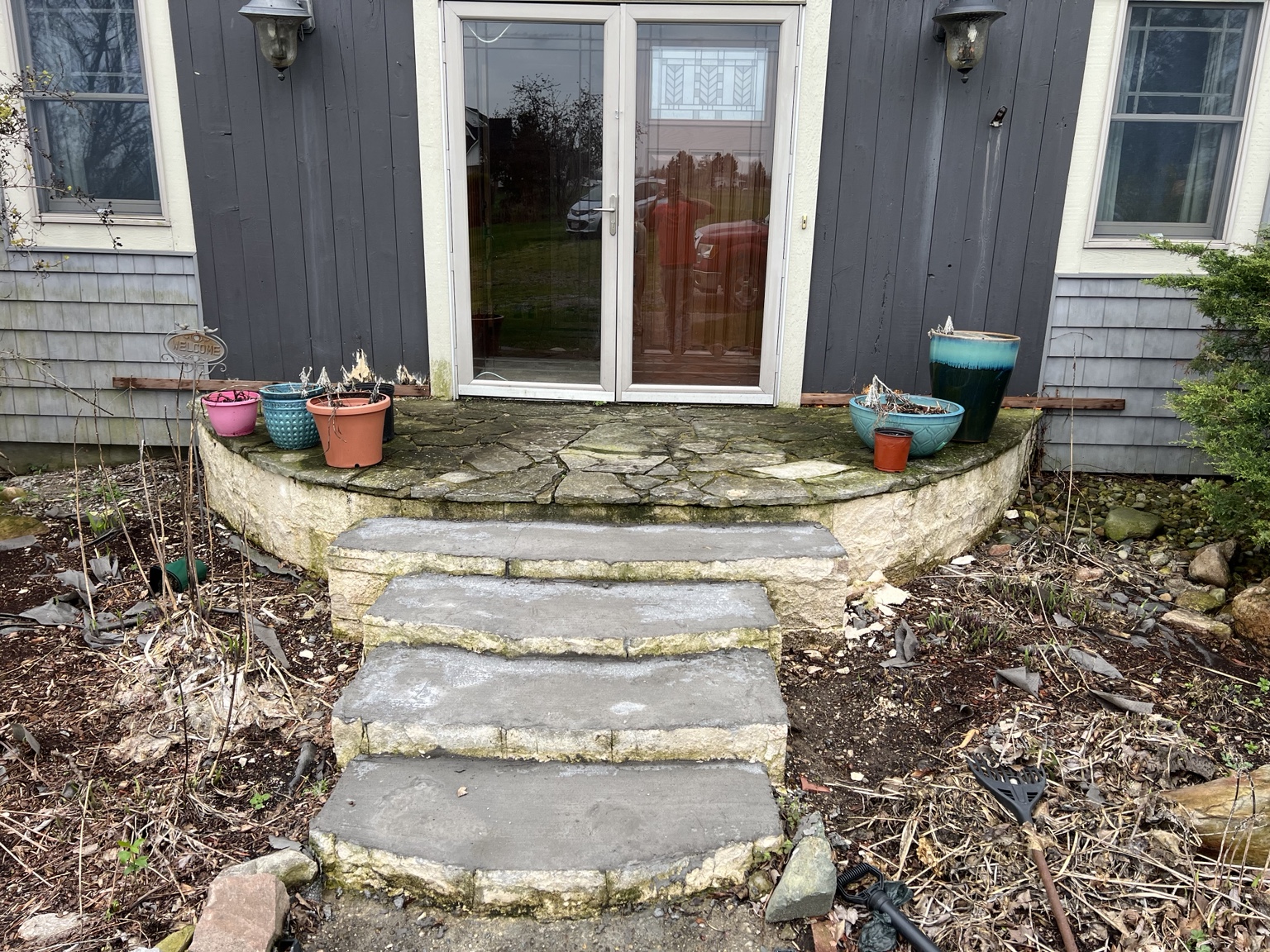 Stone landing with open joints outside red double doors, before the entry work.