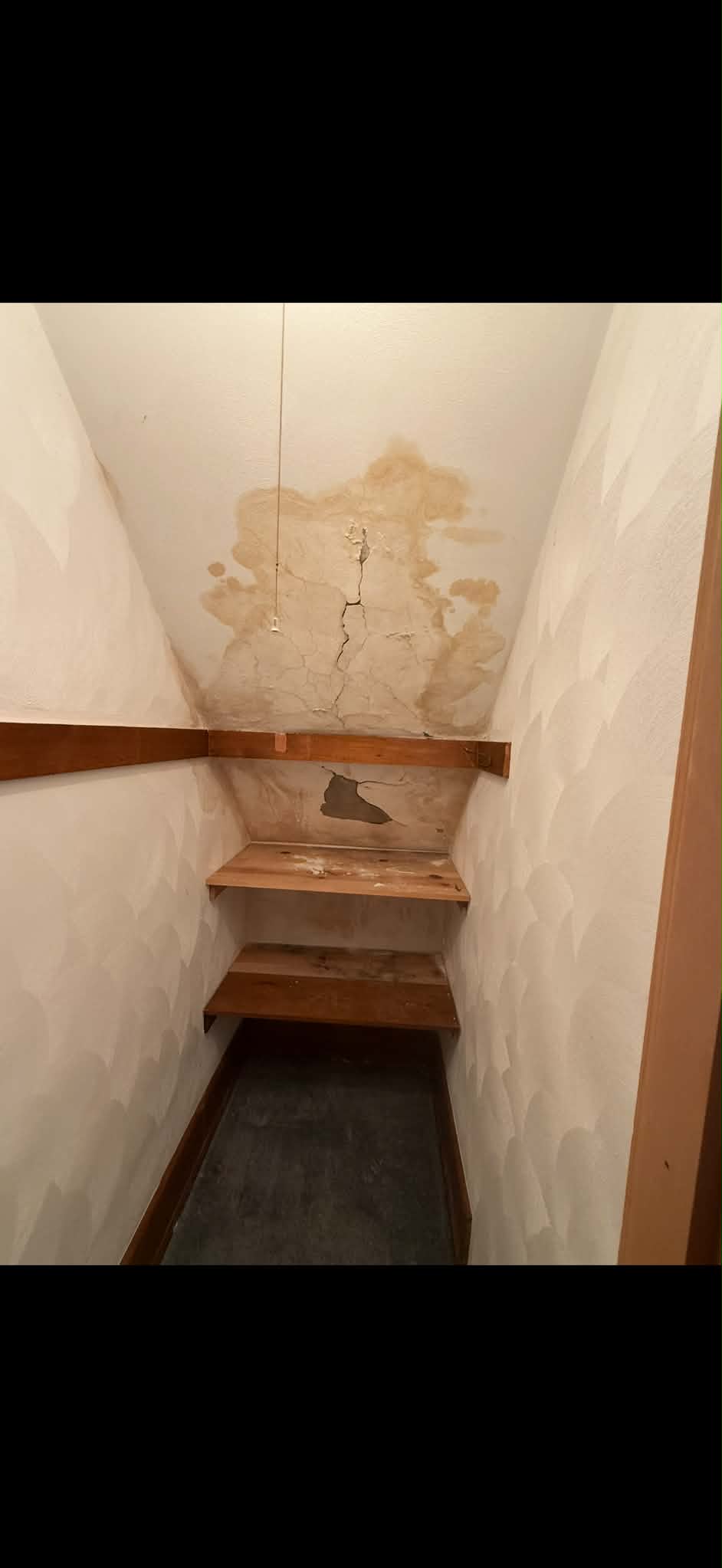 Stained and cracked plaster above the steps at the end of a narrow stairwell.